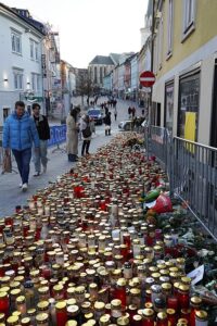 A town centre street lined with hundreds of candles and people pausing to look at them