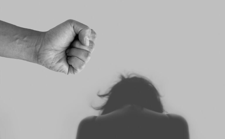 Black and white image of a fist reaching towards a woman's cowering head.